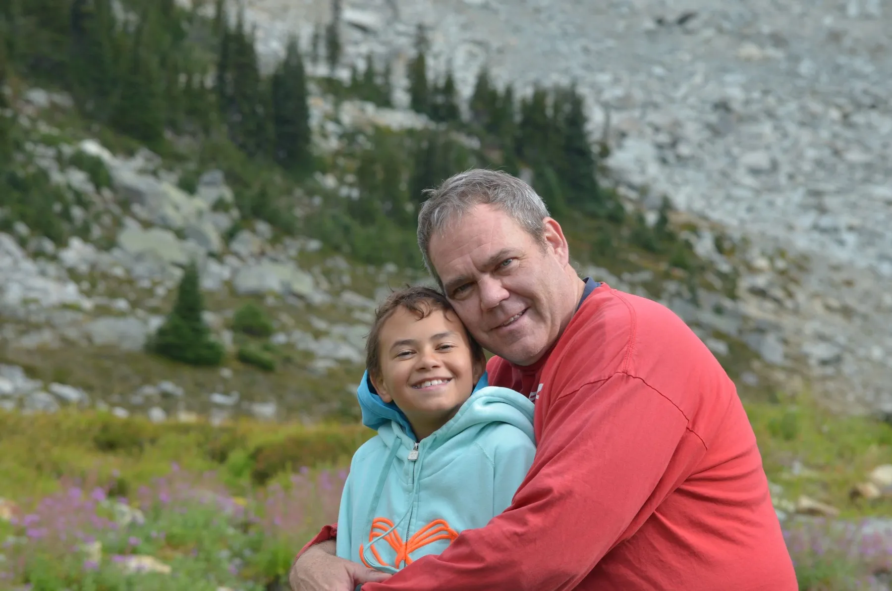 Lance and his son Jack hugging and smiling outdoors in the mountains